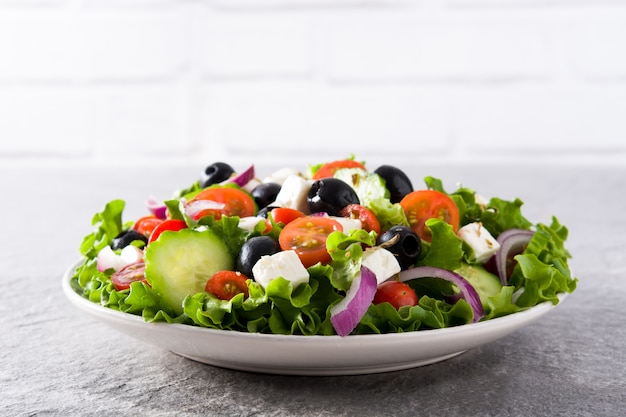 Fresh Greek salad in Plate with black olive,tomato,feta cheese, cucumber and onion on gray background