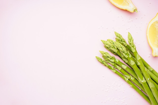 Fresh green asparagus and lemon wedges on pink surface, place for text. Flat lay.