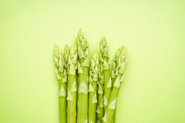 Fresh green asparagus on light green surface, close-up. Flat lay