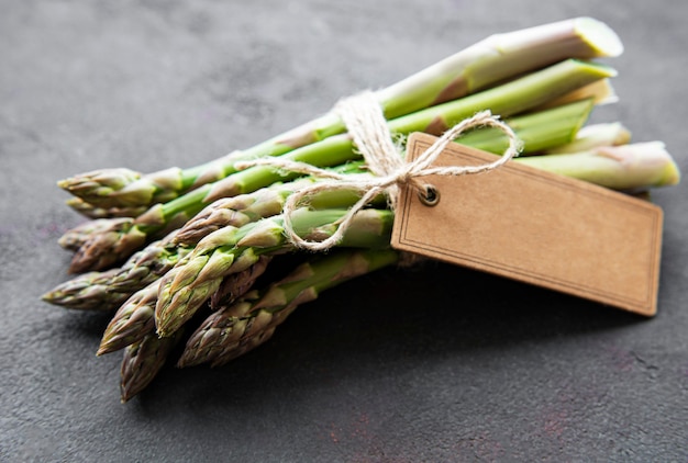 Fresh green asparagus with empty tag on black concrete background. Flat lay