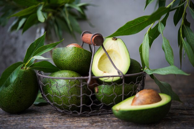 Fresh green avocado with leaves on wooden space