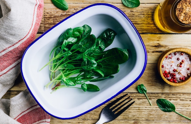 Fresh green baby spinach on plate on wooden rustic table