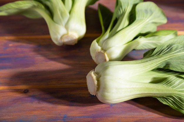 Fresh green bok choy or pac choi chinese cabbage on a colored wooden background. Hard light, contrast. Side view, close up, selective focus.