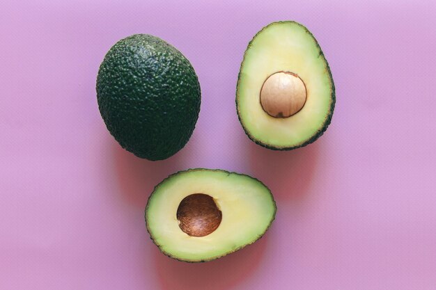 Fresh green cut in half and whole avocado isolated on a pink background, top view, close-up, space for text.