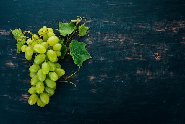 Fresh green grapes with leaves of grapes Top view On a black wooden background Free space for text