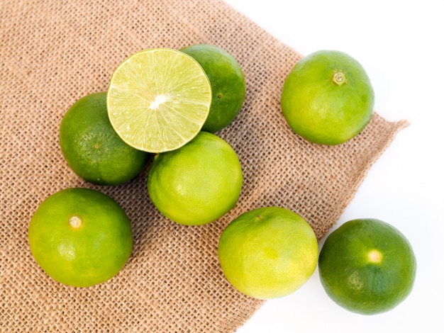 Fresh green lemons on sackcloth and fern leaves isolated on white surface.