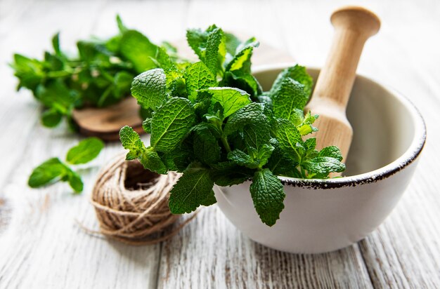 Fresh green mint in mortar on white wooden surface