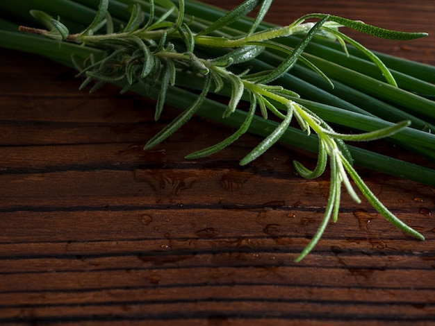 Fresh green onions and fresh rosemary on a natural wooden surface.