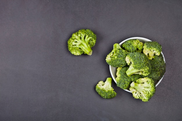 Fresh green organic broccoli in white bowl on black board.