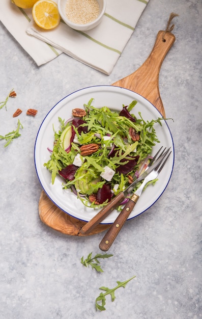 Fresh green organic  salad with arugula, beetroot  slices, feta cheese , nuts, apple on white  plate, top view. Healthy eating, dieting concept