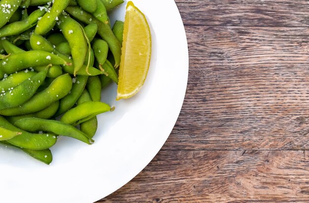 Fresh green pea pods with lemon on a wooden table.