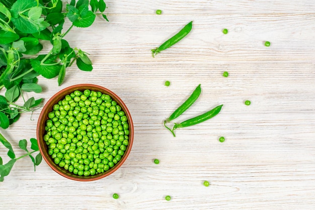 Fresh green peas in a bowl against the background of leaf green peas on a white wooden table