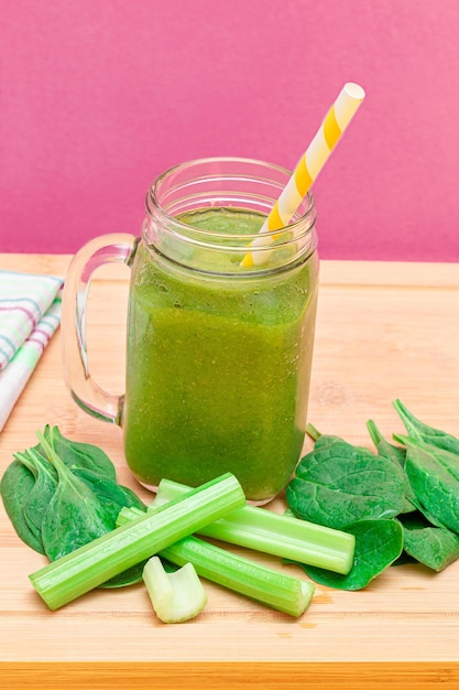 Fresh Green Smoothie of Apple Celery and Spinach in Glass Smoothie Jar with Yellow Cocktail Straw on Wooden Cutting Board Vegan Detox Drink Vegetarian Culture Healthy Eating and Fruit Diet