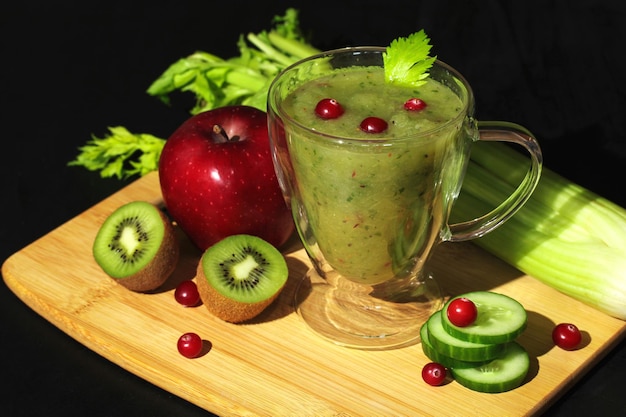 Fresh green smoothie in a glass cup with celery apple cucumber kiwi and cranberries healthy vegan drink