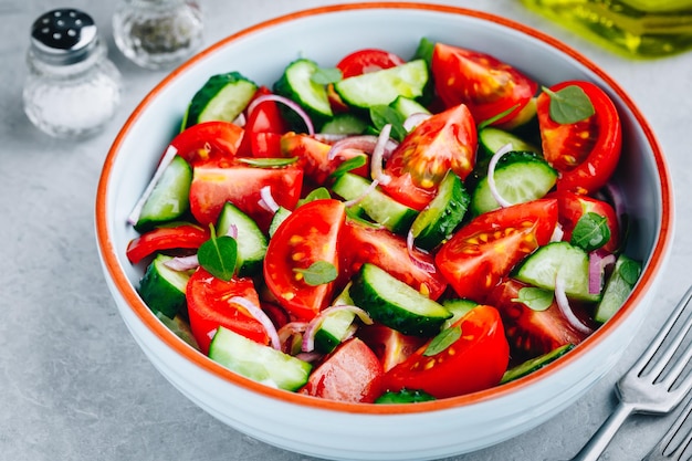 Fresh green summer salad bowl with tomatoes cucumbers red onions basil and olive oil dressing