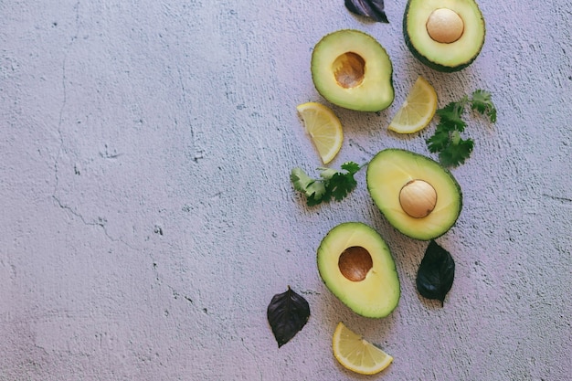 Fresh green whole, halved and sliced avocado and lemon, coriander and Basil isolated on a stone background, top view, space for text.