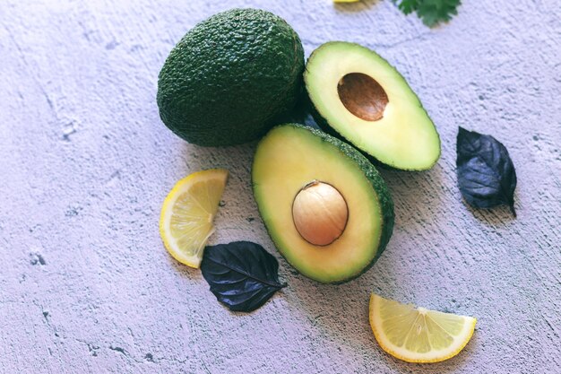 Fresh green whole, halved and sliced avocado and lemon, coriander and Basil isolated on a stone background