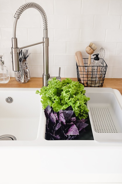 Fresh greens and basil in the white kitchen sink