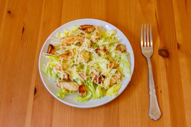 Fresh healthy caesar salad with chicken breast lettuce parmesan cheese dressing and croutons on wooden table Top view