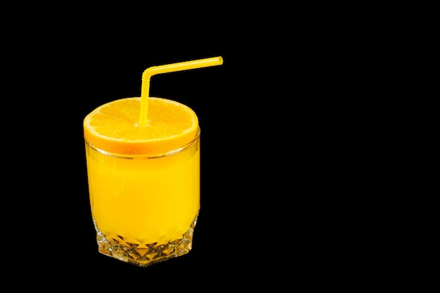 Fresh healthy orange juice in a glass with citrus cover and straw on black background