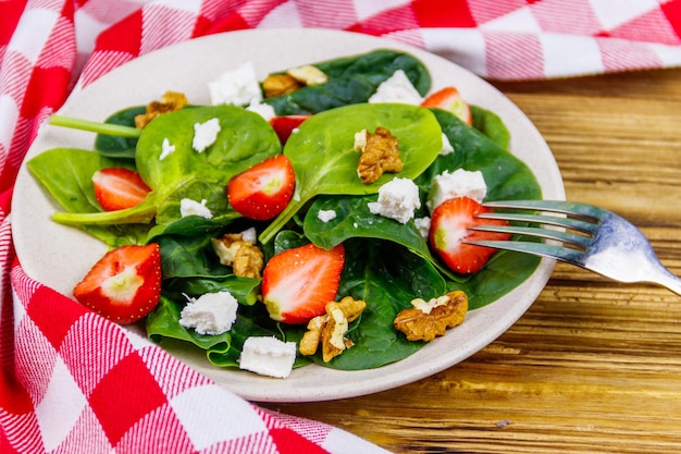 Fresh healthy salad with strawberry spinach walnuts and feta cheese on wooden table