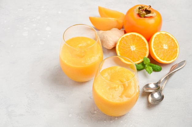 Fresh healthy smoothie with persimmon, orange and ginger on gray concrete background.