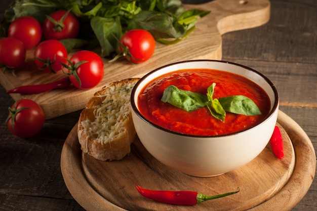 Fresh, healthy tomato soup with basil, pepper, garlic, tomatoes and bread on wooden