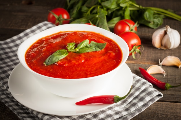 Fresh, healthy tomato soup with basil, tomatoes on wooden background. Spanish gazpacho soup.