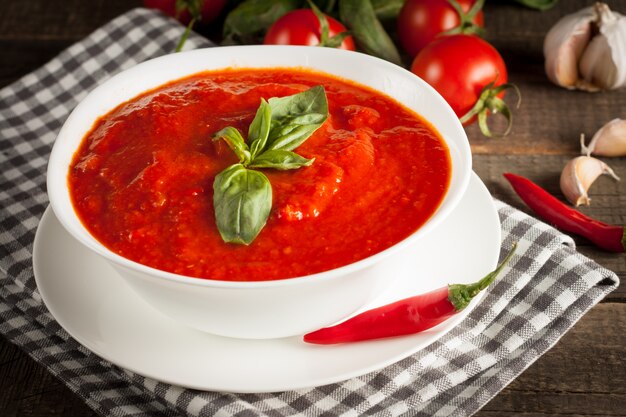 Fresh, healthy tomato soup with basil, tomatoes on wooden background. Spanish gazpacho soup.