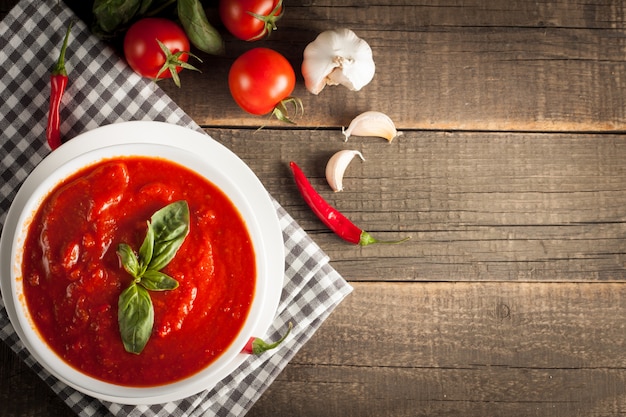 Fresh, healthy tomato soup with basil, tomatoes on wooden background. Spanish gazpacho soup.