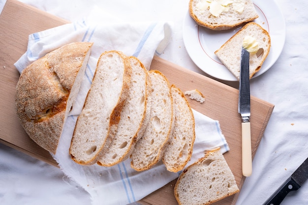 Fresh homemade baked bread and sliced bread on rustic white wooden table.