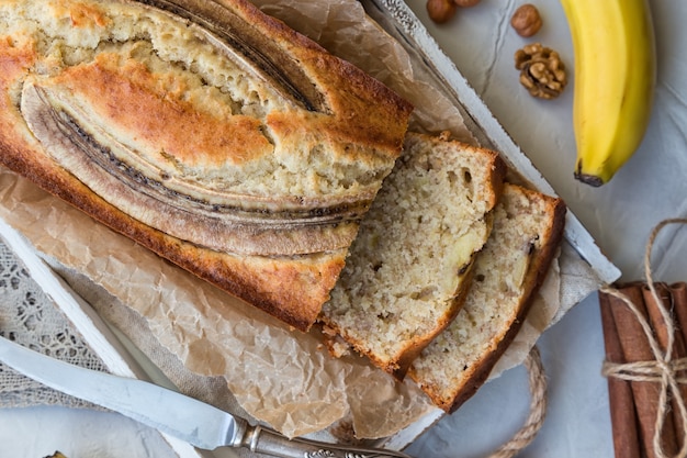 Fresh homemade banana bread in white wooden tray with ingredients on light concrete background