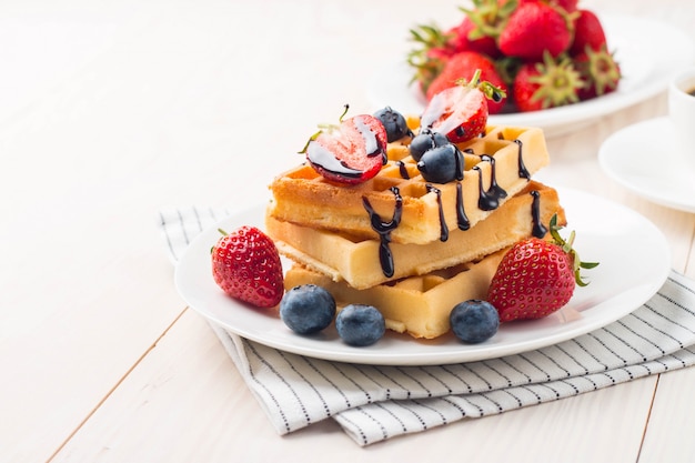 Fresh homemade Belgian waffles with chocolate syrup, strawberries, and blueberries