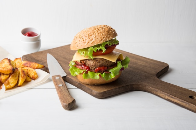 Fresh homemade burger with meat, ketchup and french fries on a light wooden background. Copy space.