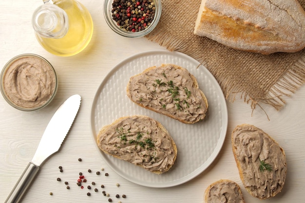 Fresh homemade chicken liver pate with herbs for bread on a white wooden table. A sandwich. top view