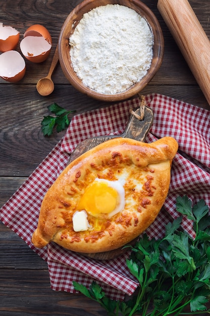 Fresh homemade khachapuri Ajarian on rustic wooden background. Dough boats filled with sulguni cheese and egg.