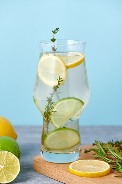 Fresh homemade lemonade with lime, mint, rosemary, thyme and ice in the glass with paper straw on blue background