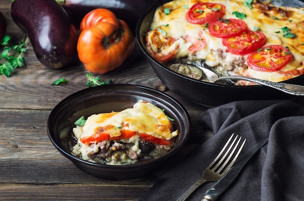 Fresh homemade moussaka in iron skillet on rustic wooden background with ingredients. Greek cuisine.