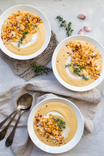 Fresh homemade roasted cauliflower and chickpea soup in bowls on light gray concrete background