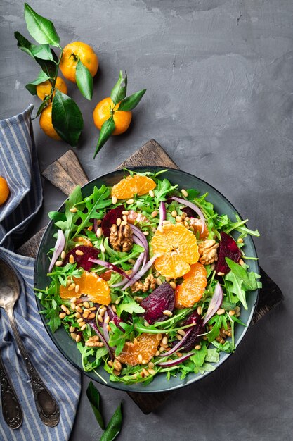 Fresh homemade tangerine and beet salad with arugula, walnuts and pine nuts on grey concrete. Healthy vegan food. Top view.