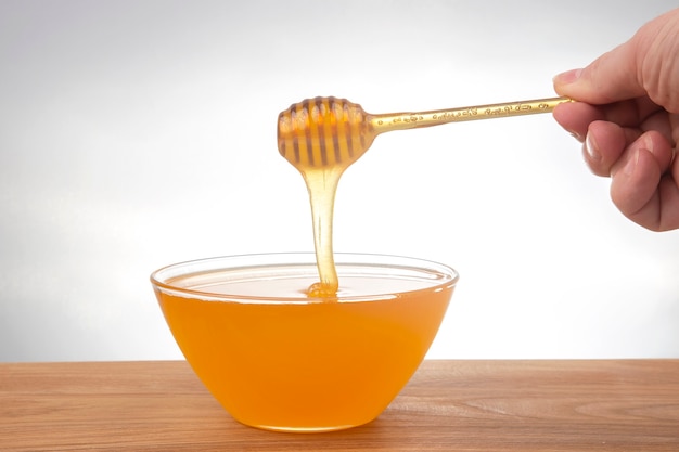 Fresh honey dripping from a spoon into a transparent plate on a white background. organic vitamin health food