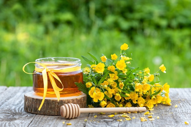 Fresh honey in a jar and yellow flowers.