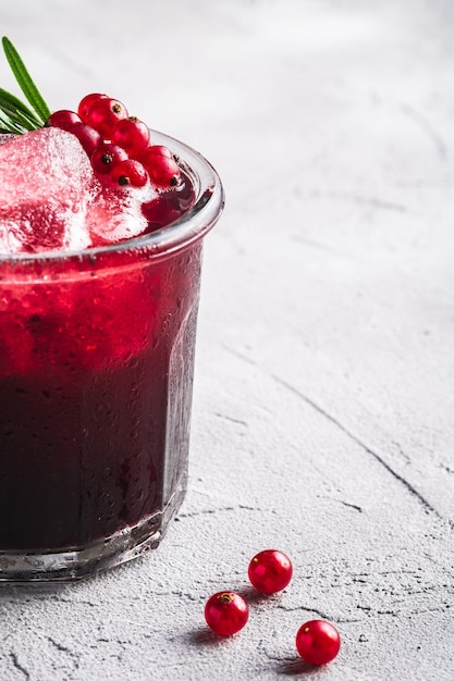 Fresh ice cold fruit cocktail in glass, refreshing summer red currant berry drink with rosemary leaf on stone concrete background, angle view