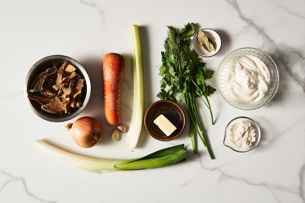 Fresh Ingredients for Classic Mushroom Soup Preparation Dried Mushrooms Carrot and Onion Garlic and Celery Leek Parsley Butter Sour Cream and Flour Arranged on Marble Counter