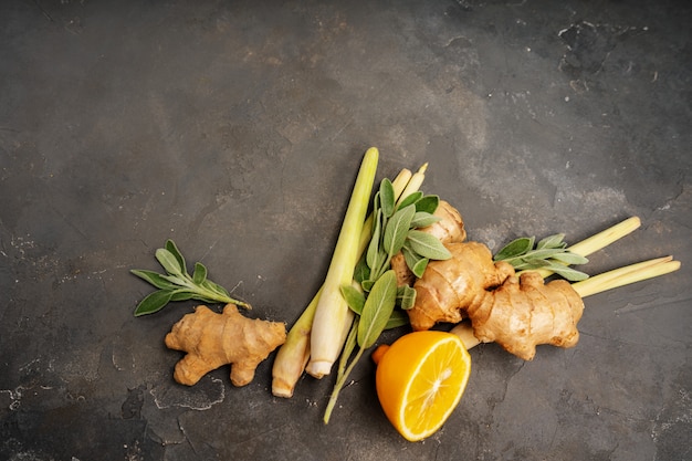 Fresh ingredients ginger, lemongrass, sage, honey and lemon for healthy antioxidant and anti-inflammatory ginger tea on dark background with copy space. Top view.