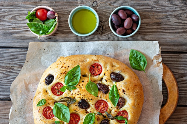 Photo fresh italian flat bread focaccia with tomatoes, olives, garlic and herbs on a wooden background.