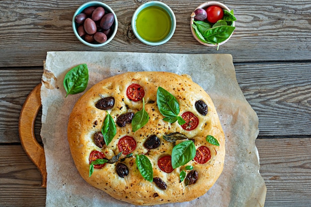 Fresh Italian flat bread Focaccia with tomatoes, olives, garlic and herbs on a wooden background.