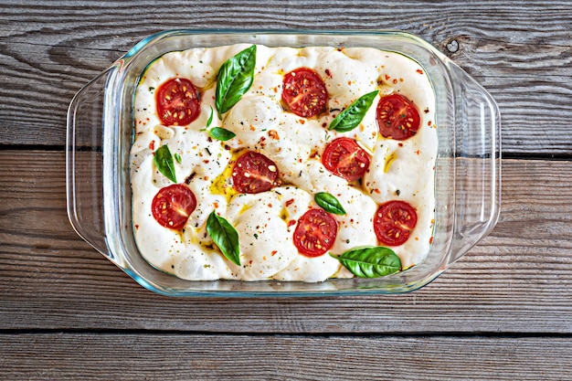 Fresh Italian flat bread (raw) Focaccia with tomatoes, olives, garlic and herbs on a wooden backgrou