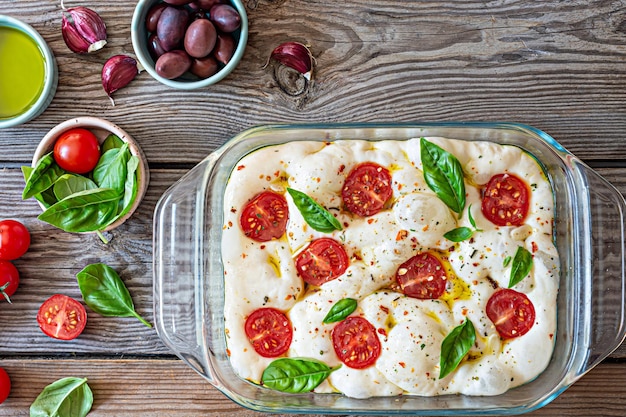 Fresh Italian flat bread (raw) Focaccia with tomatoes, olives, garlic and herbs