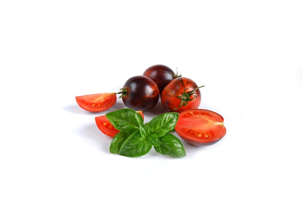 Fresh Italian green basil and red with dark whole and cut tomatoes on a white background.